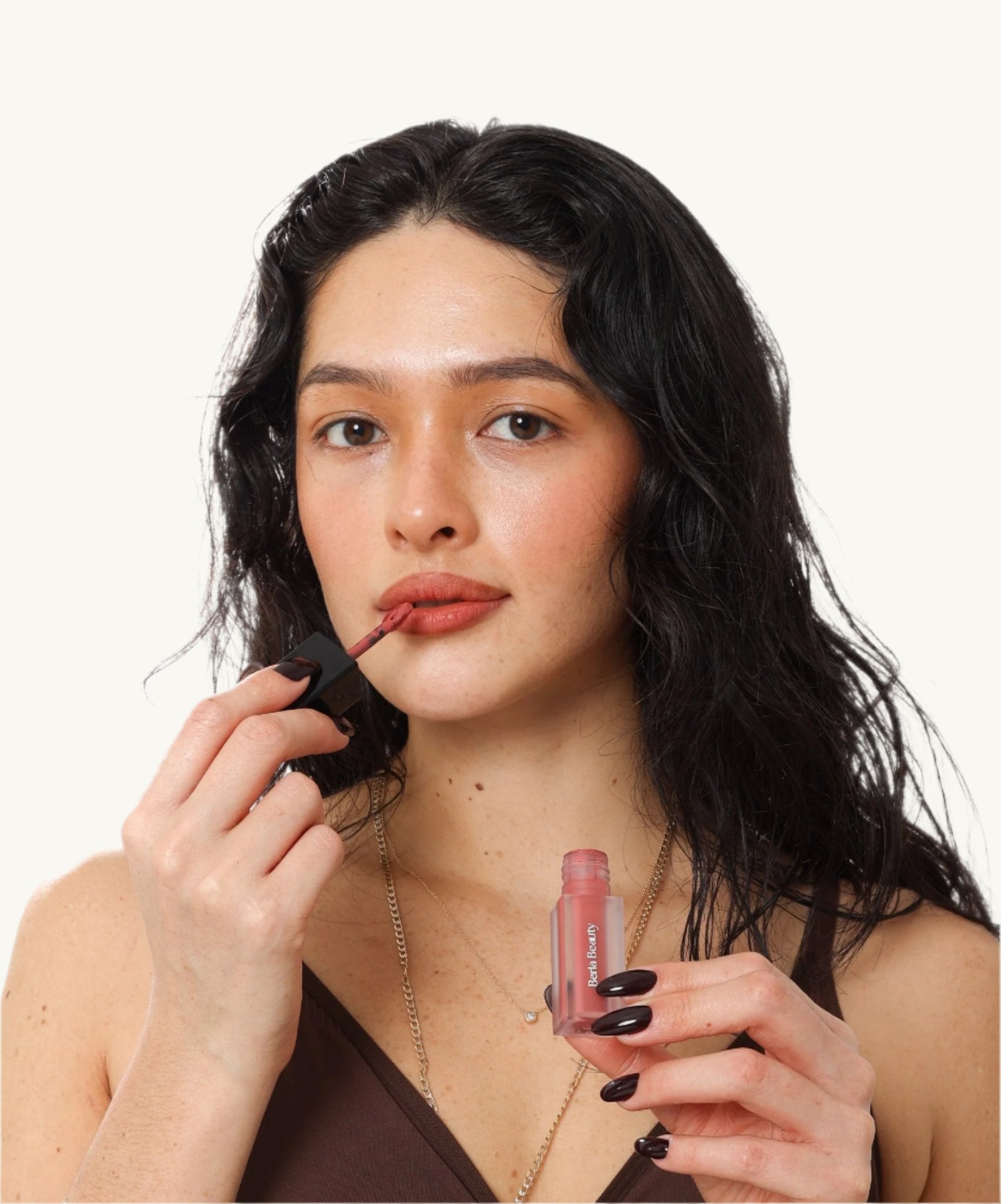 A tube of vegan-friendly Vegan Matte Lip Stain - Long Lasting, Moisturizing, and Pigment Rich from Berla Beauty stands upright against a beige background. The lipstick has a clear base displaying the product color and a black rectangular cap. The brand name is printed vertically in white on the front of the tube.