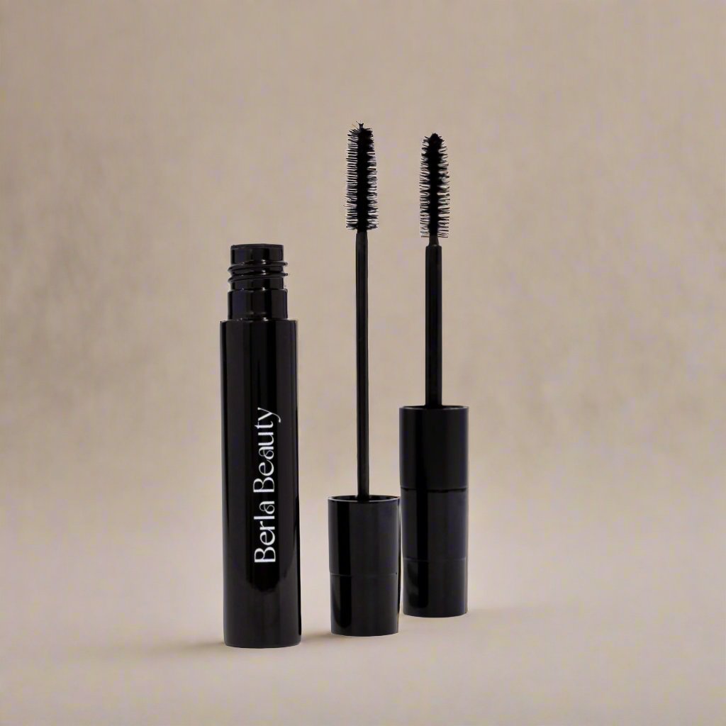 A close-up image showcases a black mascara tube labeled "Berla Beauty" in white. The Vegan Dual Lash Long Lasting Mascara - Bold and Beautiful Lashes is open, with one wand attached to the cap and another standing beside it. The background is a plain, light-colored surface.